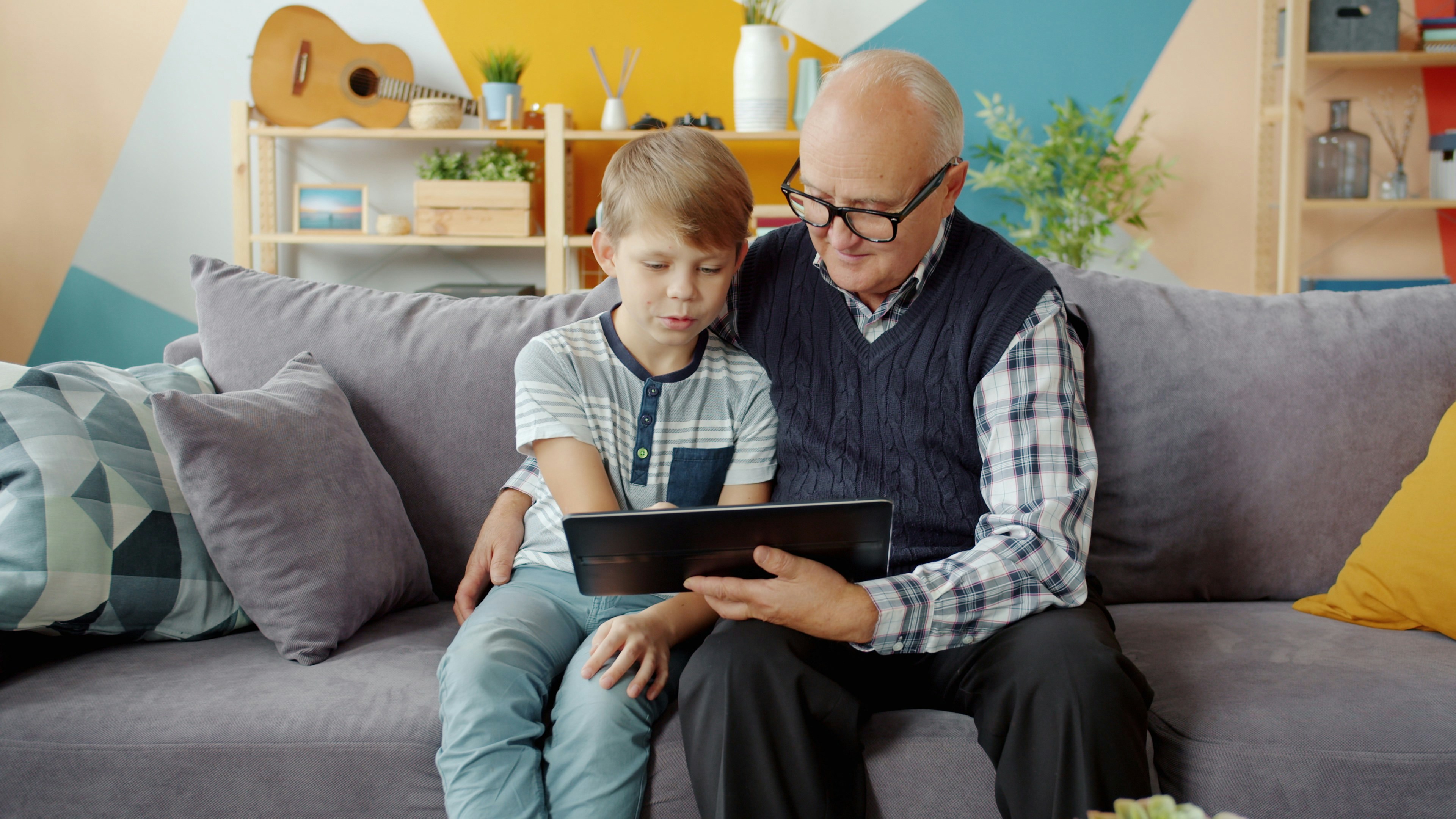 Un enfant et son grand-père regardent l'écran de la tablette.