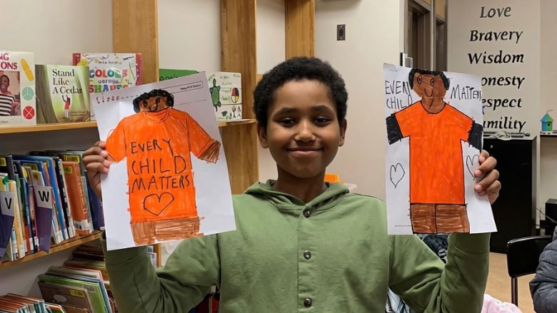 Un enfant participant à un cercle de lecture autochtone, montrant son dessin de chandails orange pour la Journée nationale de la vérité et de la réconciliation.