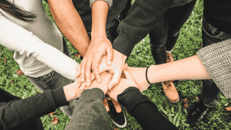 Des mains multiples qui se rejoignent dans un geste uni, comme pour un cri de ralliement ou d’encouragement, symbolisant le travail d’équipe et la solidarité.