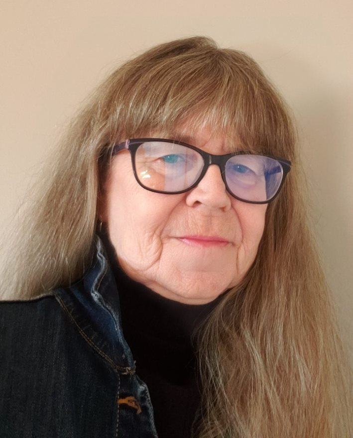 A woman with brown hair, black glasses, and a black turtleneck.